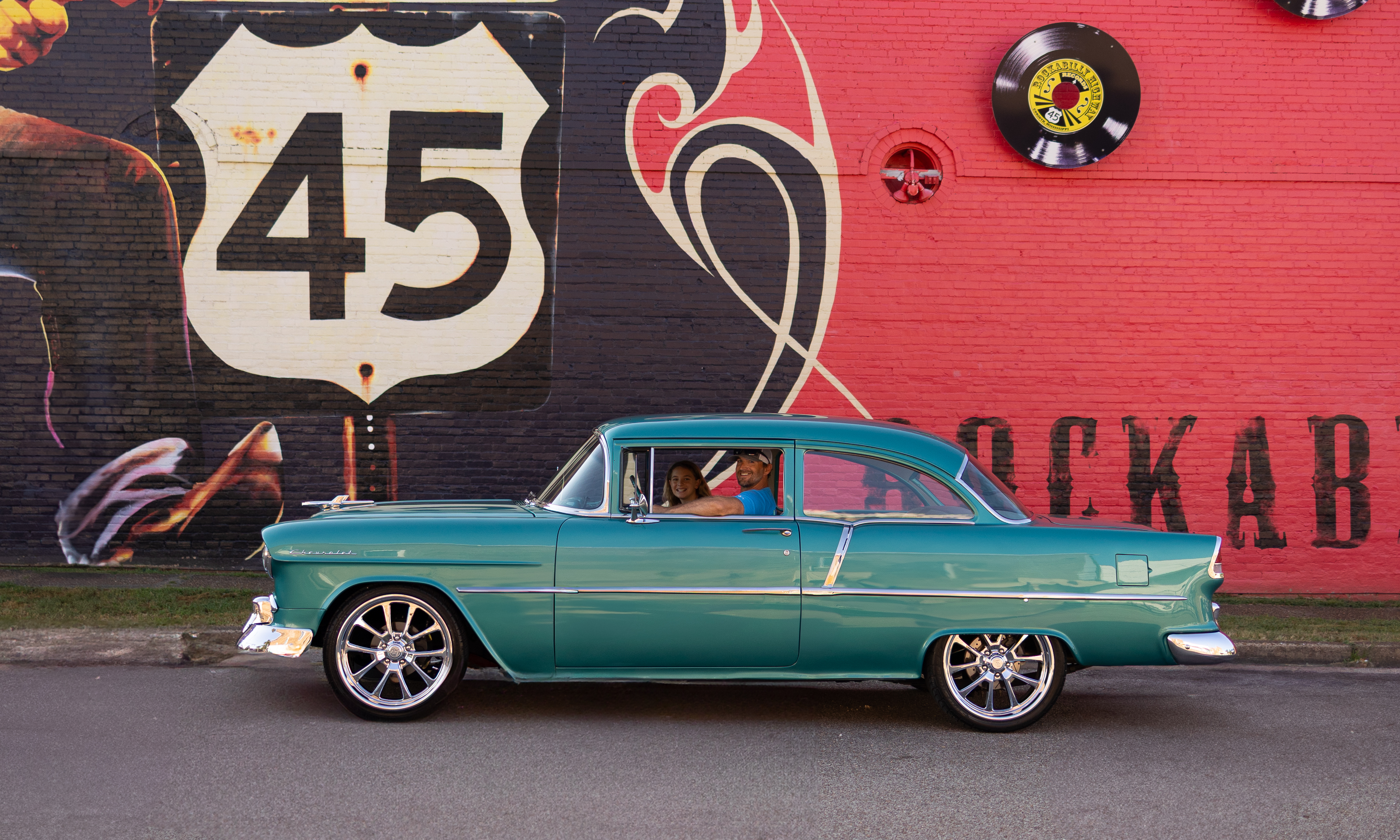 Teal classic car rolling past the Route 45 Rockabilly Highway mural in downtown Selmer